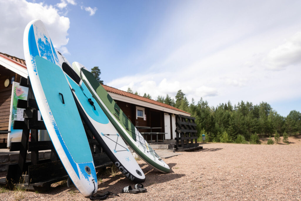 Kolme sup-lautaa odottamassa käyttäjiä Melliläjärven rantakahvilan edustalla aurinkoisessa säässä.