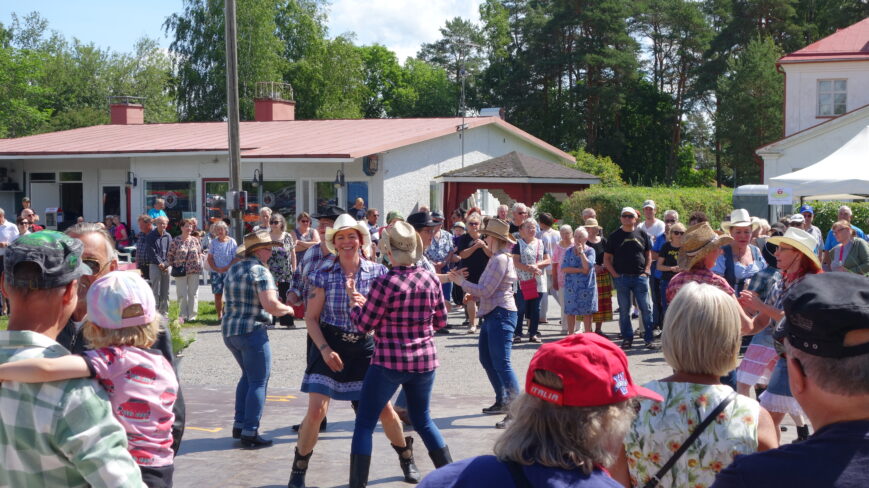 Kuva kylätapahtumasta, jossa tapahtumaväki katsoo rivitanssijoiden esitystä.